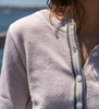 Close up of Noyac Knits Lynn crop cardigan in premium light tan Egyptian cotton with signature grosgrain ribbon trim in stripes of army green, tan, light blue and white wit mother of pearl buttons.