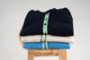 Noyac Knits premium cotton crew neck cardigans with ribbon trim in navy, tan and French blue shown folded on a stool on white background. These cardigans can be worn in early fall and as summer to fall transition pieces.