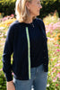 Woman in garden setting wearing Julie classic cardigan in navy merino with ribbon trim in stripes of navy, white and navy over matching sleeveless shell in navy merino.