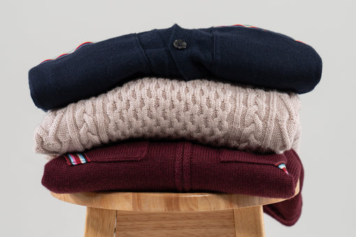 stack of men's sweater on stool on plain background in burgundy, beige and navy colors from Noyac Knits