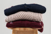 stack of men's sweater on stool on plain background in burgundy, beige and navy colors from Noyac Knits