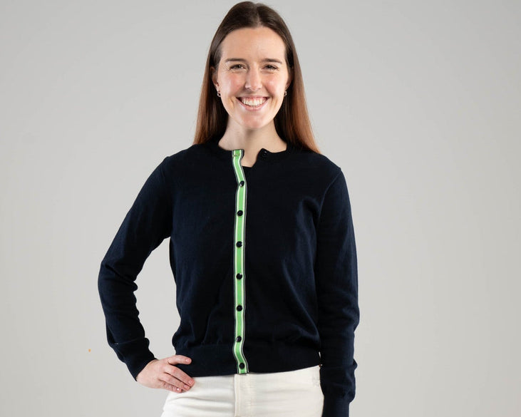 woman wearing navy ribbon cardigan with green, white and navy striped ribbon trim on plain background