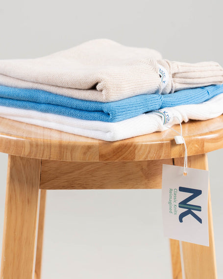 stack of cotton sweaters with noyac knits hang tag showing on wooden bench