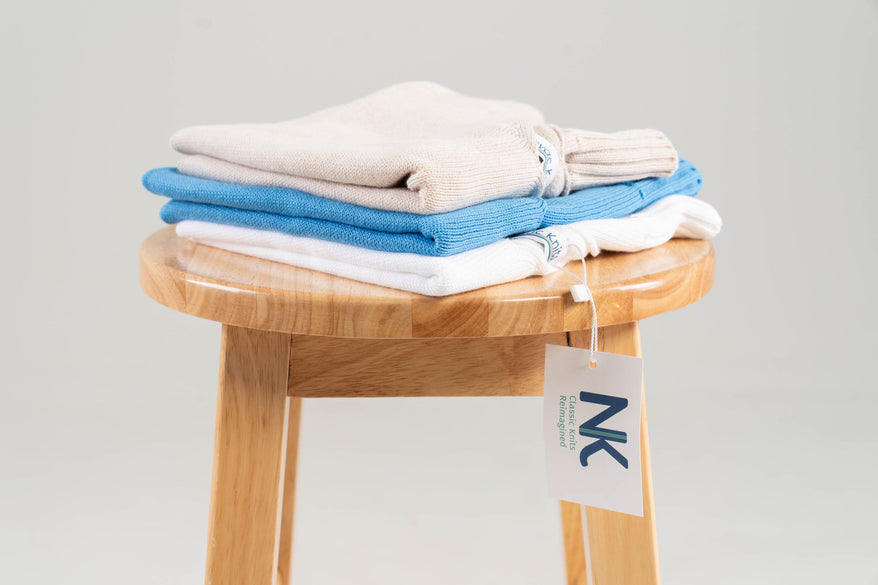 stack of cotton sweaters with noyac knits hang tag showing on wooden bench