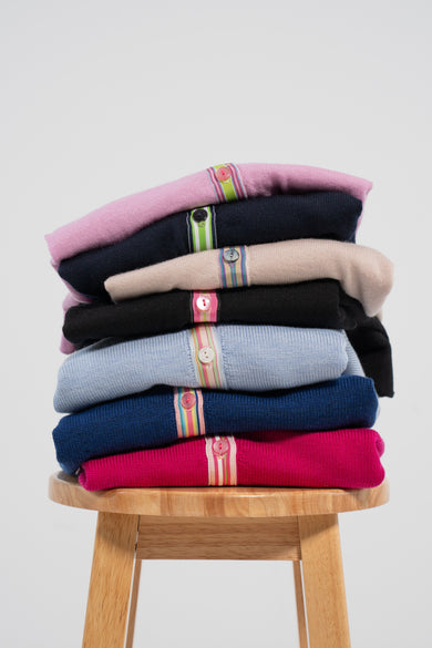 Stack of colorful cardigans on wood stool and plain background.