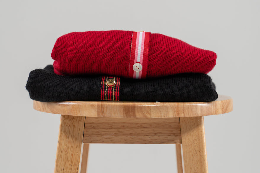 red and black sweater stacked on wood stool with plain background