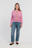Picture of woman wearing Noyac Knits orchid pink cardigan with pink buttons and  signature ribbon trim in stripes of green, pink and lilac -- knit in ultrasoft premium merino wool, styled with pearl choker necklace, jeans, and ballet flats on plain bakckground.