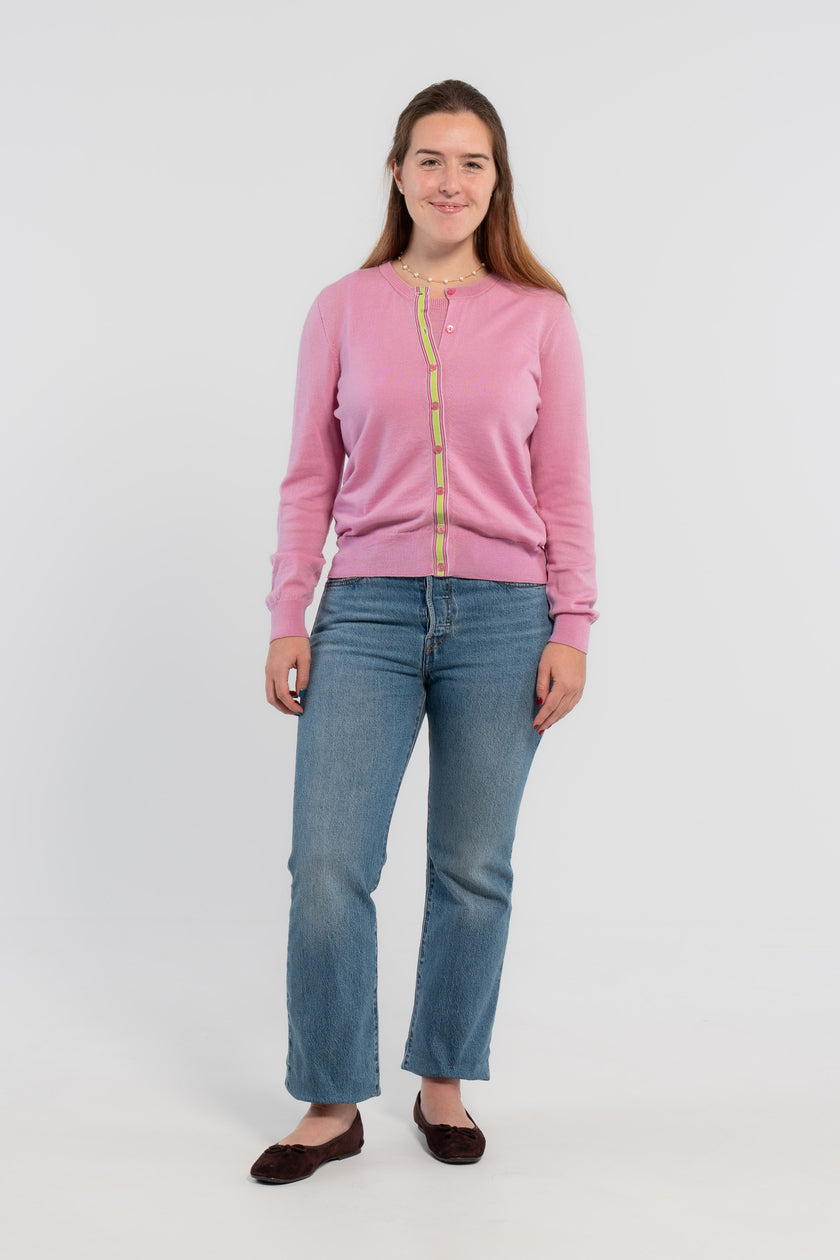 Picture of woman wearing Noyac Knits orchid pink cardigan with pink buttons and  signature ribbon trim in stripes of green, pink and lilac -- knit in ultrasoft premium merino wool, styled with pearl choker necklace, jeans, and ballet flats on plain bakckground.