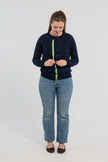 Woman wearing  Noyac Knits Julie classic cardigan in navy trimmed with signature  navy buttons and green, white and navy grosgrain ribbon -- knit in premium, lightweight merino -- over matching navy shell sweater, also in soft merino, and styled with jeans and ballet flats on plain background.