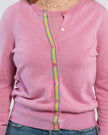 Close up of woman wearing orchid pink cardigan with pink buttons and green, pink and lavender stripe grosgrain ribbon trim, jeans, pearl choker necklace and plain background.