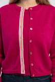Close up of woman wearing unbuttoned raspberry pink crop cardigan from Noyac Knits with signature pink buttons and pink, white and green striped grosgrain ribbon trim over matching raspberry pink sweater shell and jeans.