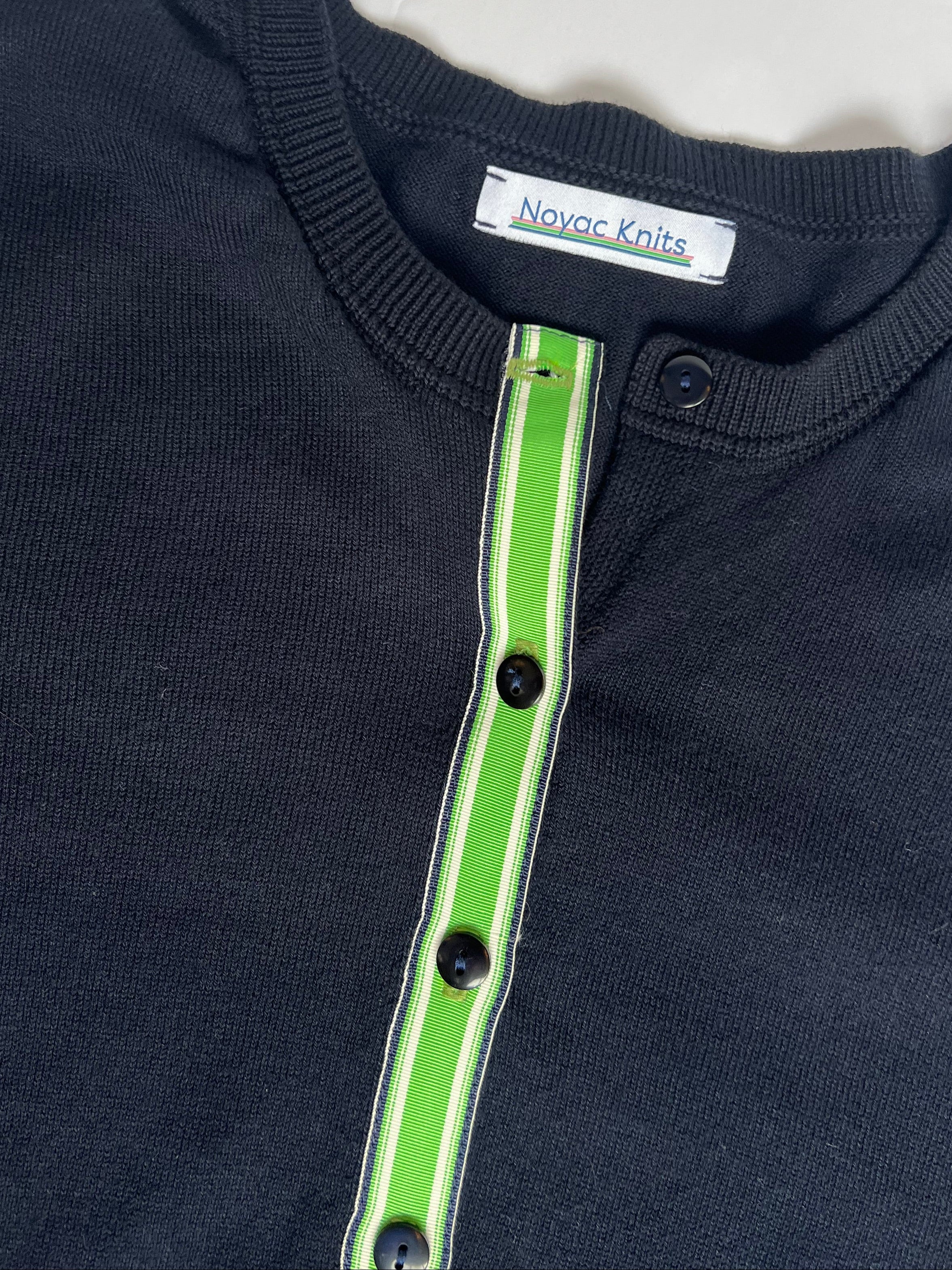 Close up of Noyac Knits navy cotton cardigan trimmed with  kelly green, white and navy ribbon with navy buttons.