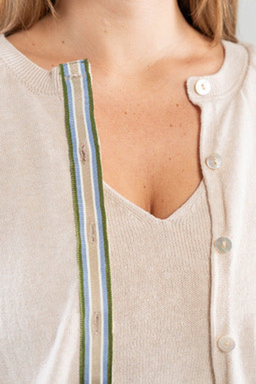 Close-up of a person wearing a light tan cardigan with a army green, light blue, white, and tan striped ribbon trim and shell buttons over v-neck tan shell sweater