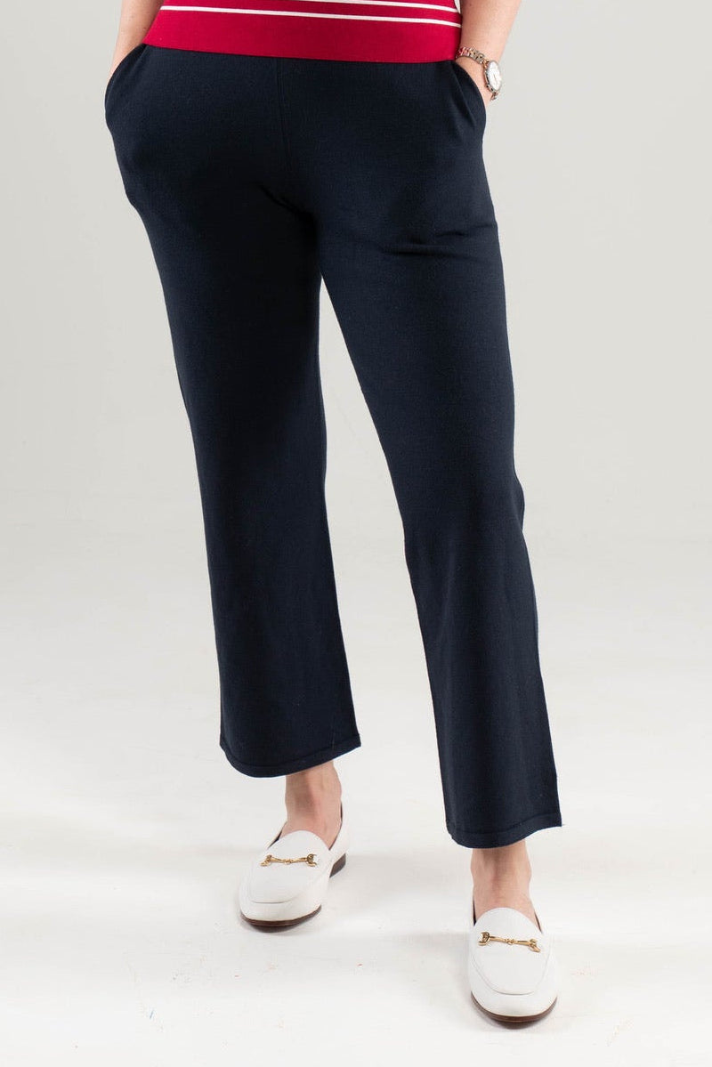 Close up of woman wearing Noyac Knits navy stretch knit ankle length pants in environmentally sustainable ecoviscose styled with red and white striped tank top and white loafers on white  background