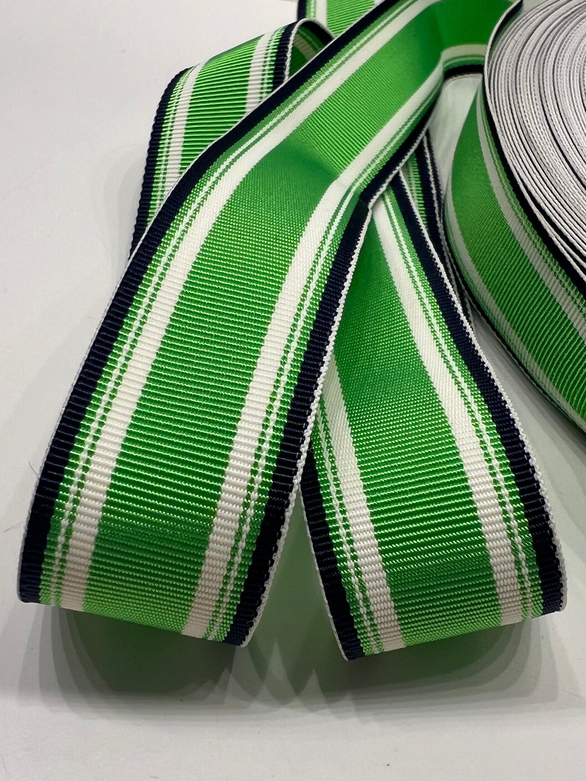 Close up of kelly green, white and navy striped grosgrain ribbon on white background