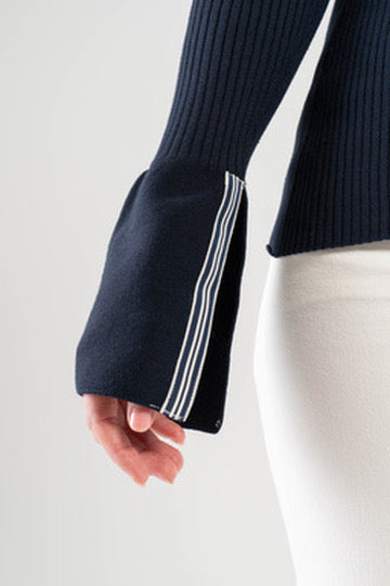Close up of elongated sleeve with navy and white striped ribbon trim on Noyac Knits wrap cardigan worn by a woman on a plain background