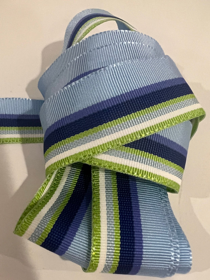 close up of ribbon with light blue, cobalt blue, navy, light green and white stripes on plain background