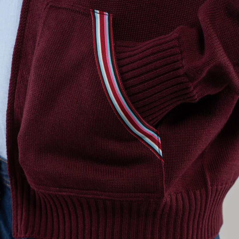 Close up of pocket on Noyac Knits burgundy bomber style sweater with signature ribbon trim in stripes in burgundy, navy, light blue, pink and white.