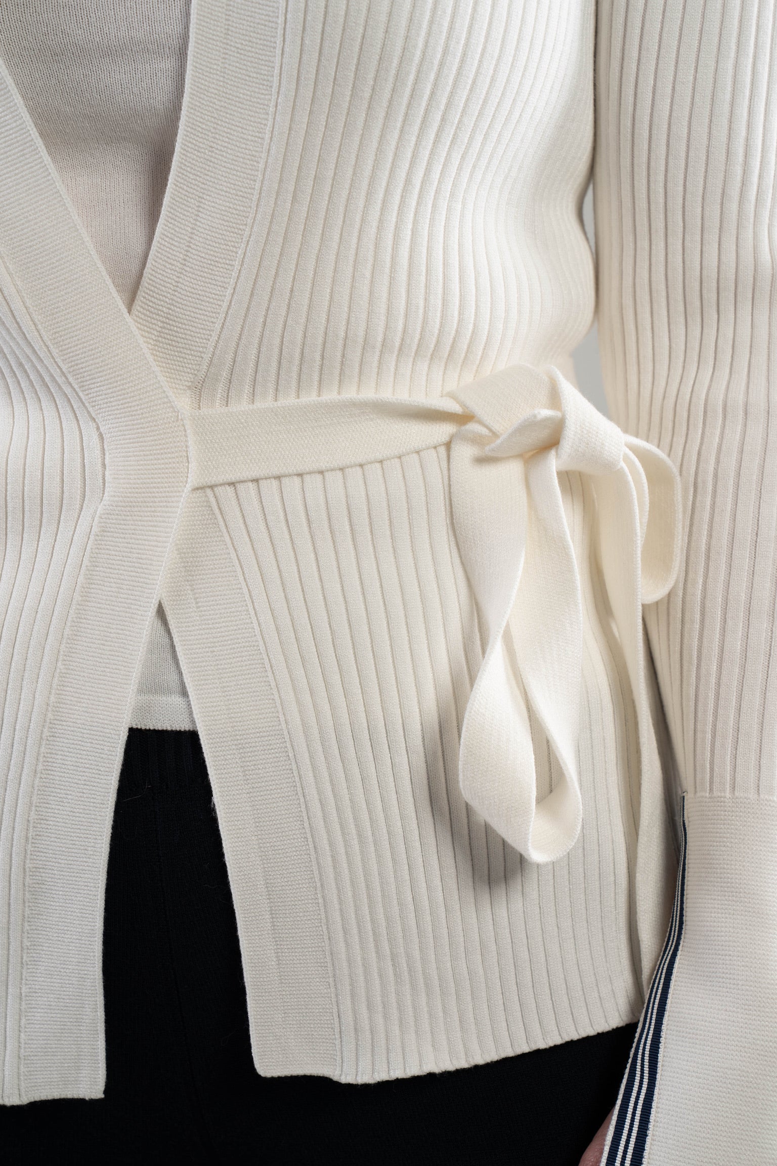 Close-up of a white ribbed knit cardigan with a self-tie