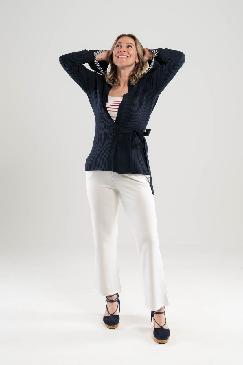 Woman wearing Noyac Knits navy wrap ribbed sweater over red and white striped square neck top styled with white pants and navy espadrilles against a plain background