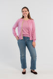 Picture of woman wearing Noyac Knits orchid pink cardigan with pink buttons and  signature ribbon trim in stripes of green, pink and lilac -- knit in ultrasoft premium merino wool, styled with pearl choker necklace, jeans, and ballet flats on plain bakckground.