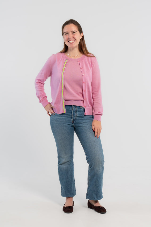 Picture of woman wearing Noyac Knits orchid pink cardigan with pink buttons and  signature ribbon trim in stripes of green, pink and lilac -- knit in ultrasoft premium merino wool, styled with pearl choker necklace, jeans, and ballet flats on plain bakckground.