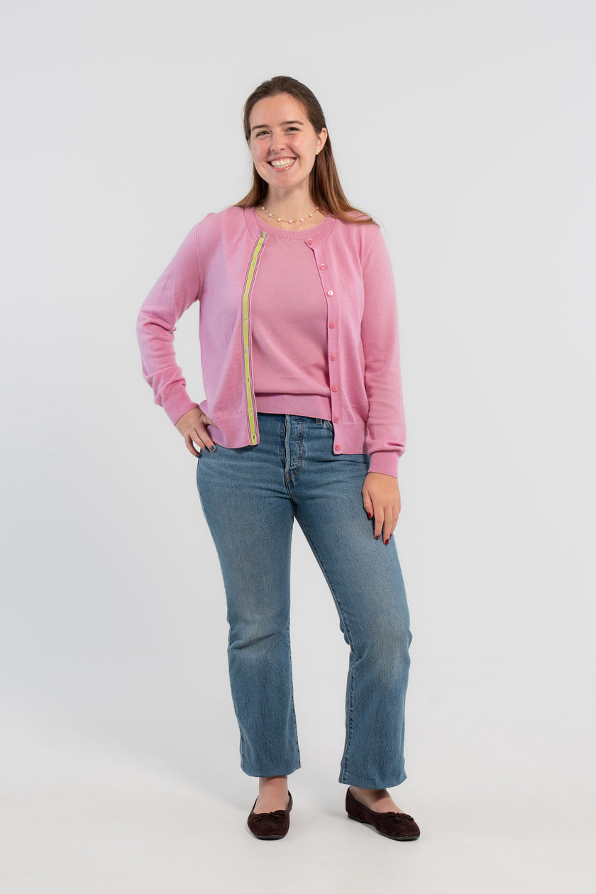 Picture of woman wearing Noyac Knits orchid pink cardigan with pink buttons and  signature ribbon trim in stripes of green, pink and lilac -- knit in ultrasoft premium merino wool, styled with pearl choker necklace, jeans, and ballet flats on plain bakckground.