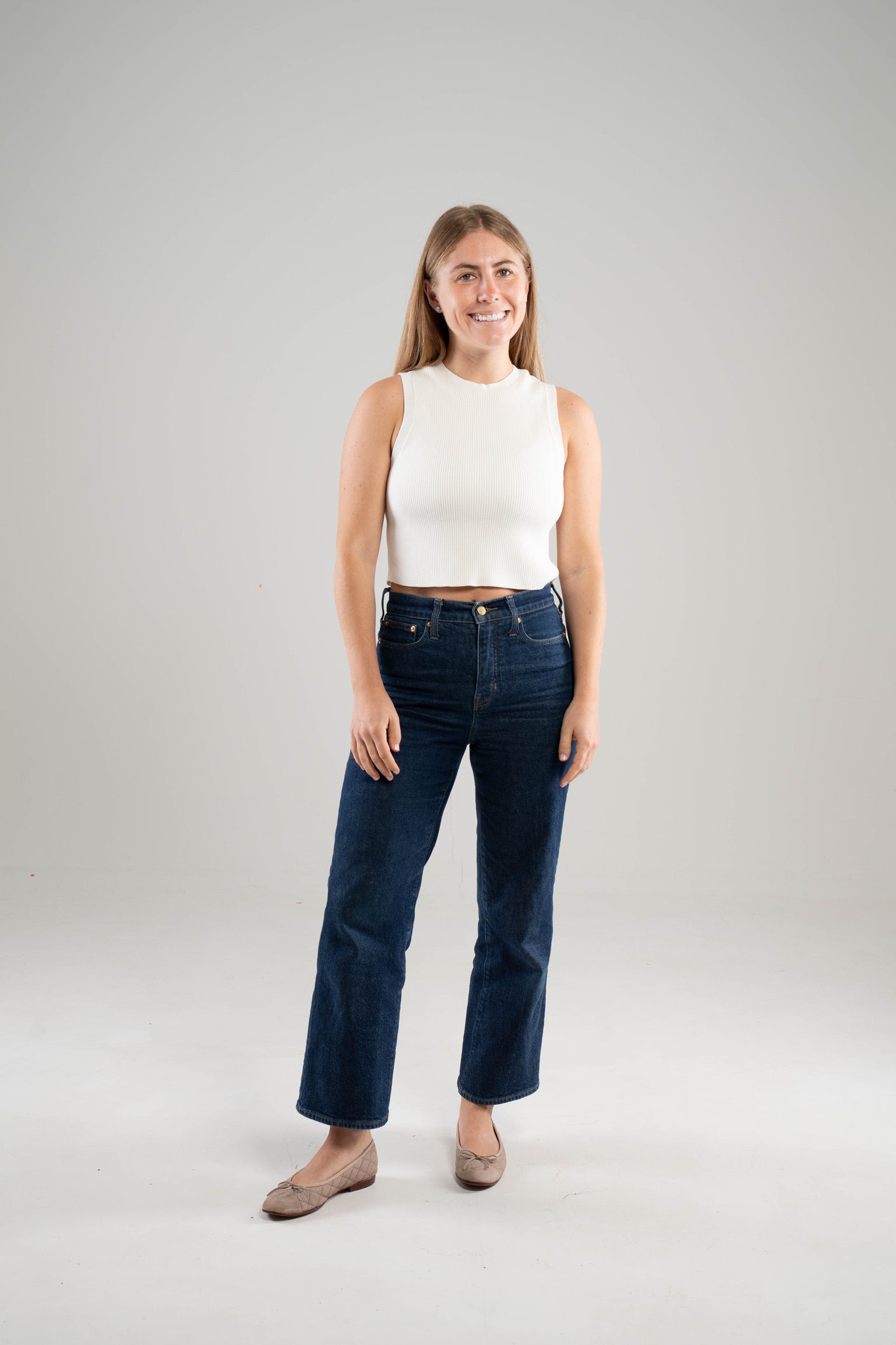 Woman wearing a Noyac Knits white sleeveless crew neck crop  top in environmentally sustainable ecoviscose styled with  dark blue jeans and ballet flats on a white background