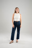 Woman wearing a Noyac Knits white sleeveless crew neck crop  top in environmentally sustainable ecoviscose styled with  dark blue jeans and ballet flats on a white background