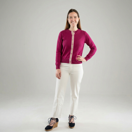 Woman wearing Noyac Knits Grace classic cardigan in beautiful raspberry pink with signature ribbon trim and pink buttons -- knit in lightweight premium merino -- styled with white jeans and espadrilles on a gray background