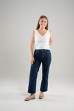 Woman wearing a Noyac Knits white cotton double v-neck crop tank top styled with dark blue jeans and ballet flats on a white  background