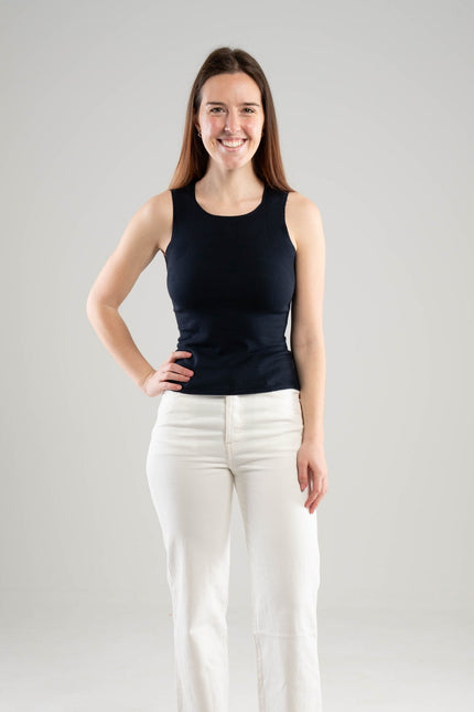 Woman wearing a Noyac Knits navy scoop neck tank top in lightweight and soft ecoviscose styled with white pants on a white  background