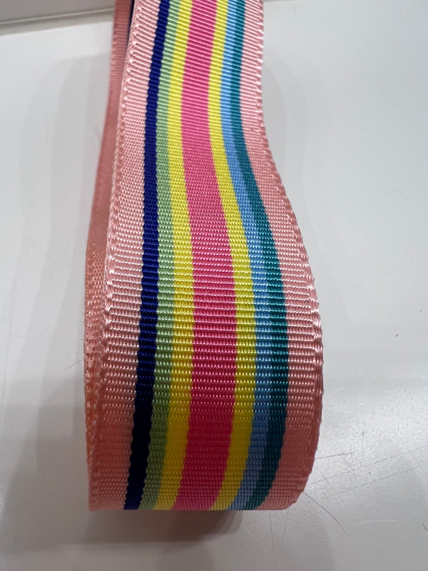 Close up of grosgrain ribbon with rainbow stripes in light pink, hot pink, light blue, teal, lemon yell, bright green and cobalt on a plain background.