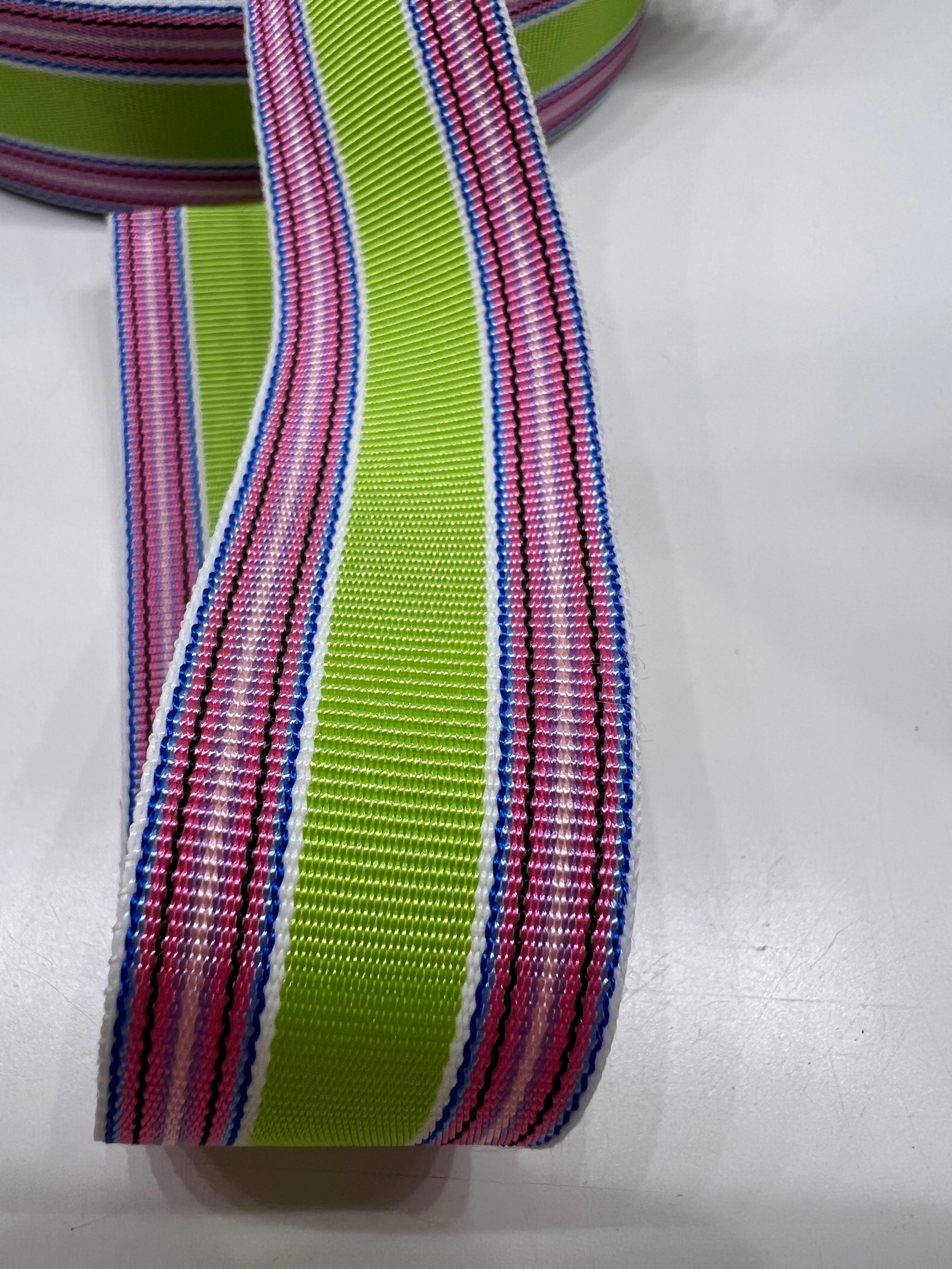 Close up of grosgrain ribbon with spring green center stripe inside thinner stripes of white, blue, dark pink, light pink, lilac, and black on plain background.