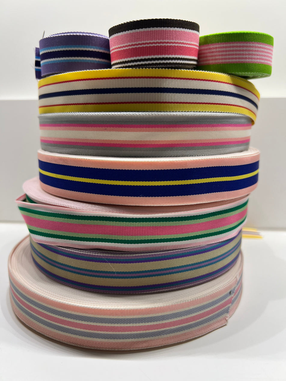 Picture of stacked spools of brightly striped grosgrain ribbon on plain background