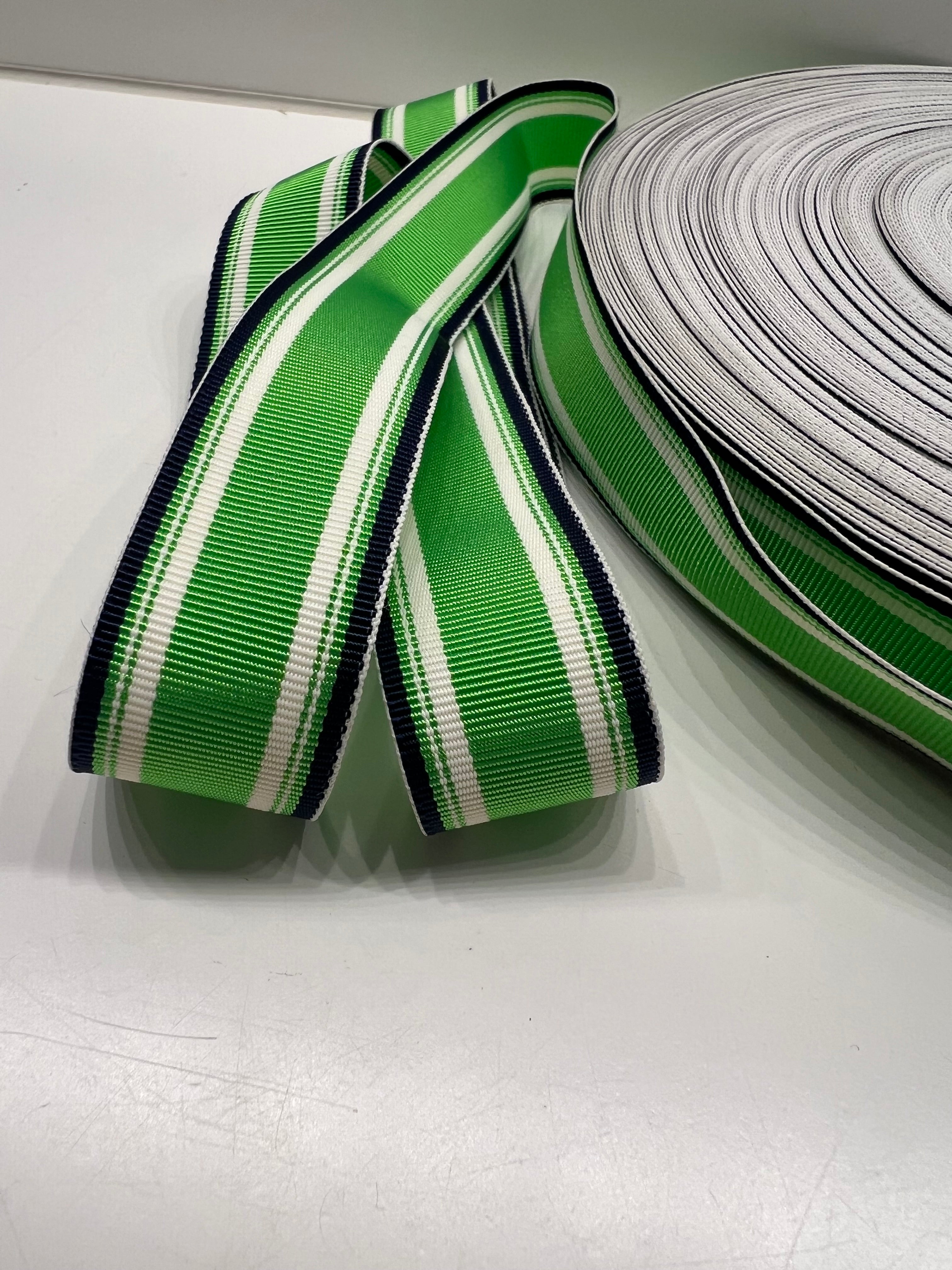 Close up of grosgrain ribbon with bright green center stripe inside thinner white, bright green and navy stripes on plain background.