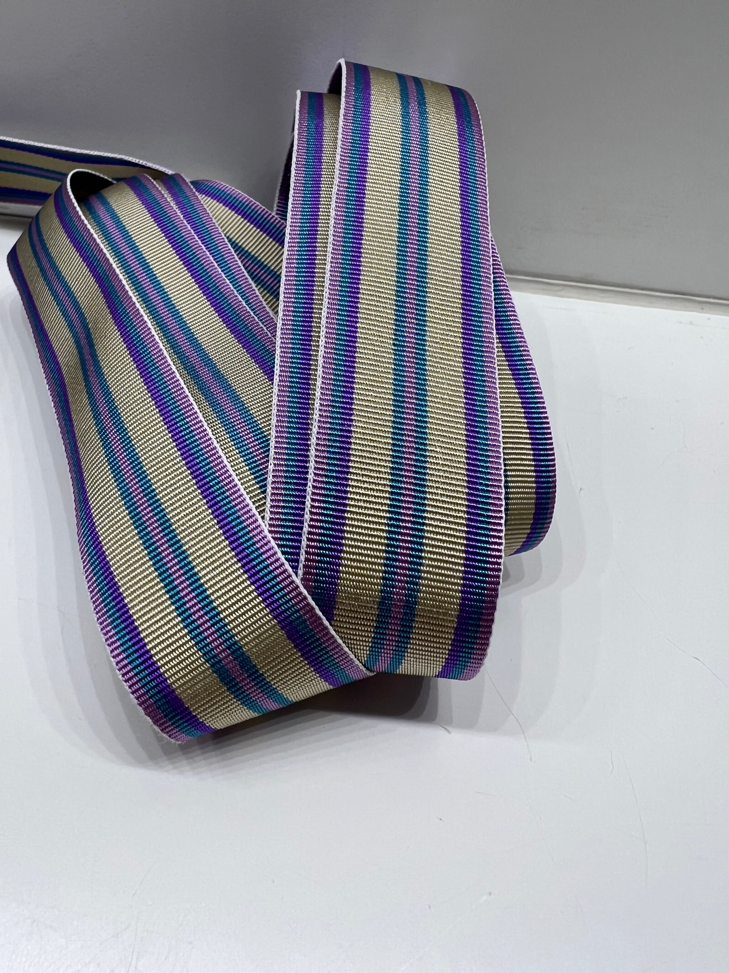 Close up of grosgrain ribbon with stripes in purple, teal, lavender and tan on plain background.