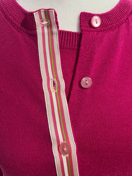 Close-up of a pink cardiga with buttons and a striped ribbon trim on a light background