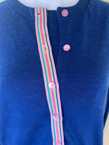 clkose up of blue cardigan with pink buttons and a rainbow-striped ribbon trim.