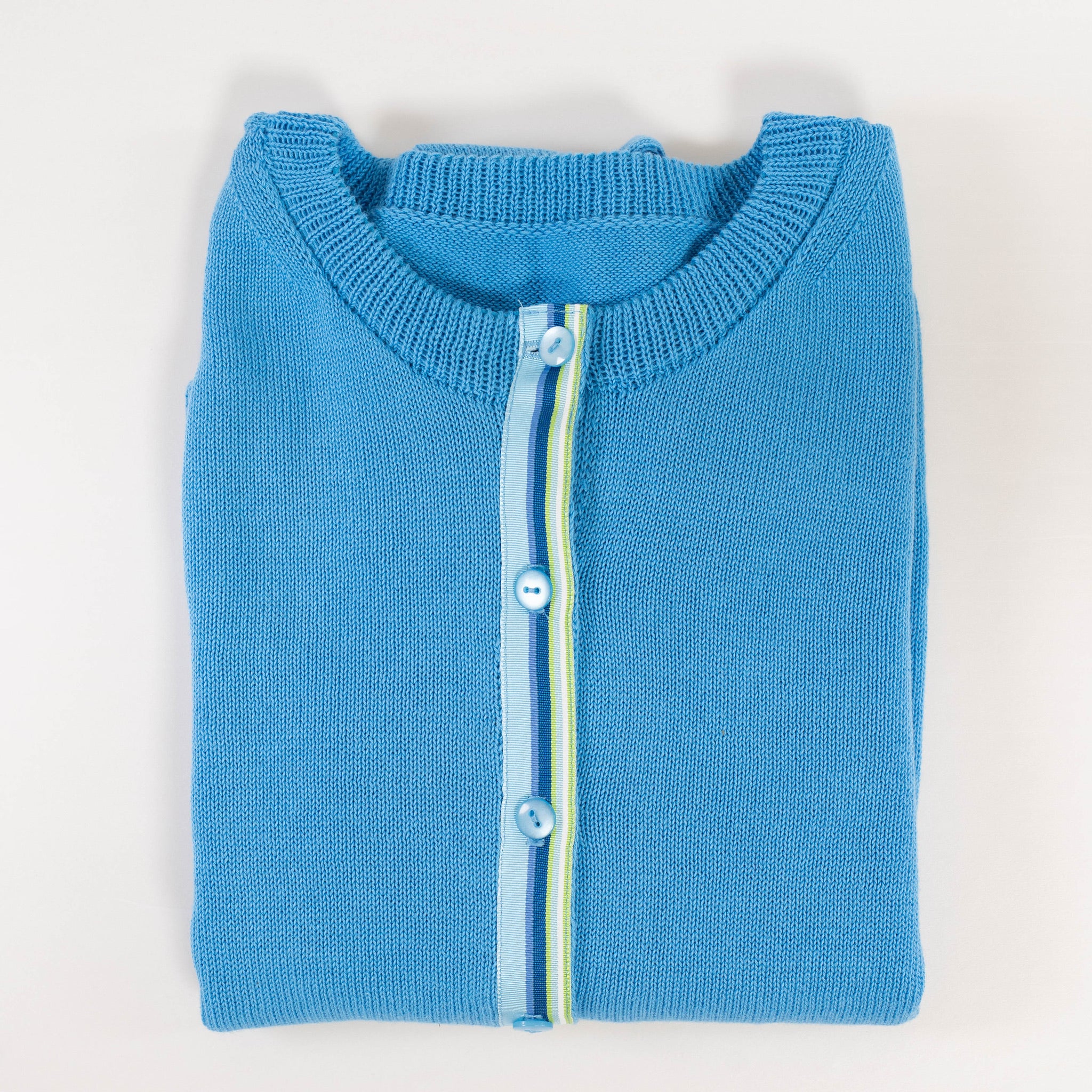 Folded Noyac Knitws French blue ribbon cardigan with a ribbon striped in blues and greens and light blue buttons made in breathable premium cotton on a light gray background