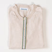 Close-up of Noyac Knits light tan cardigan with a army green, light blue, white, and tan striped ribbon trim and shell buttons over v-neck tan shell sweater on white background