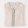 Close-up of Noyac Knits light tan cardigan with a army green, light blue, white, and tan striped ribbon trim and shell buttons over v-neck tan shell sweater on white background