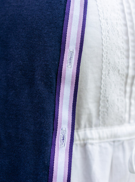 Close up of navy cardigan with striped ribbon trim in purple, lavender and white over white lace dress