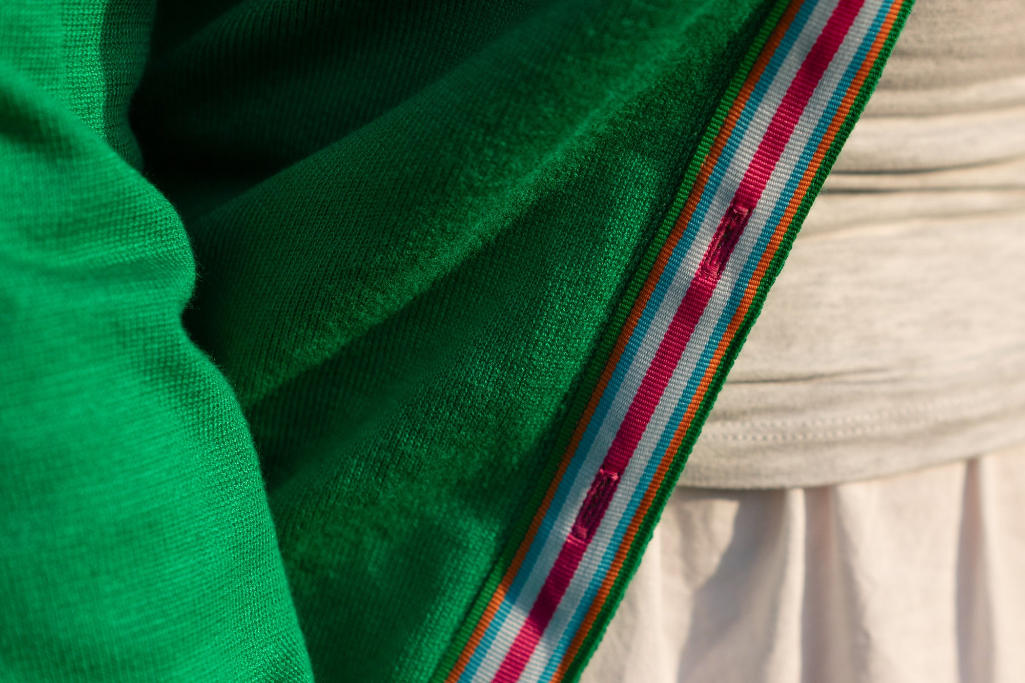 Close up of kelly green sweater with striped ribbon trim in bright pink, white, blue and orange stripes