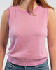 Close up of woman wearing orchid pink sleeveless sweater, jeans, pearl choker n plain background.