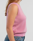 Sideview of woman wearing orchid pink sleeveless sweater, jeans, pearl choker neckless on plain background.