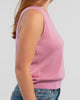 Sideview of woman wearing orchid pink sleeveless sweater, jeans, pearl choker neckless on plain background.