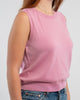 Close up of woman wearing orchid pink sleeveless sweater, jeans, pearl choker neckless on plain background.