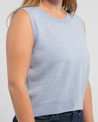 Close up of woman wearing light blue crop sleeveless sweater and jeans on plain background.