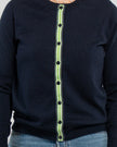 Close up of buttoned navy cardigan with navy pearlized buttons and navy, green and white striped grosgrain ribbon trim.